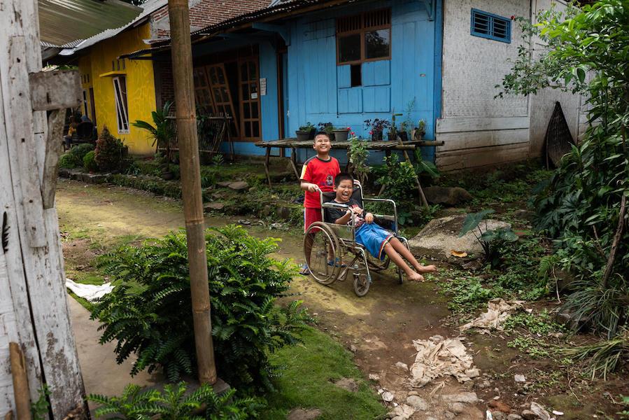 Kevin, 9, a child with a visual impairment, pushes his 12-year-old friend Syaiful's wheelchair as they play outside in Banyumas, Central Java, Indonesia.
