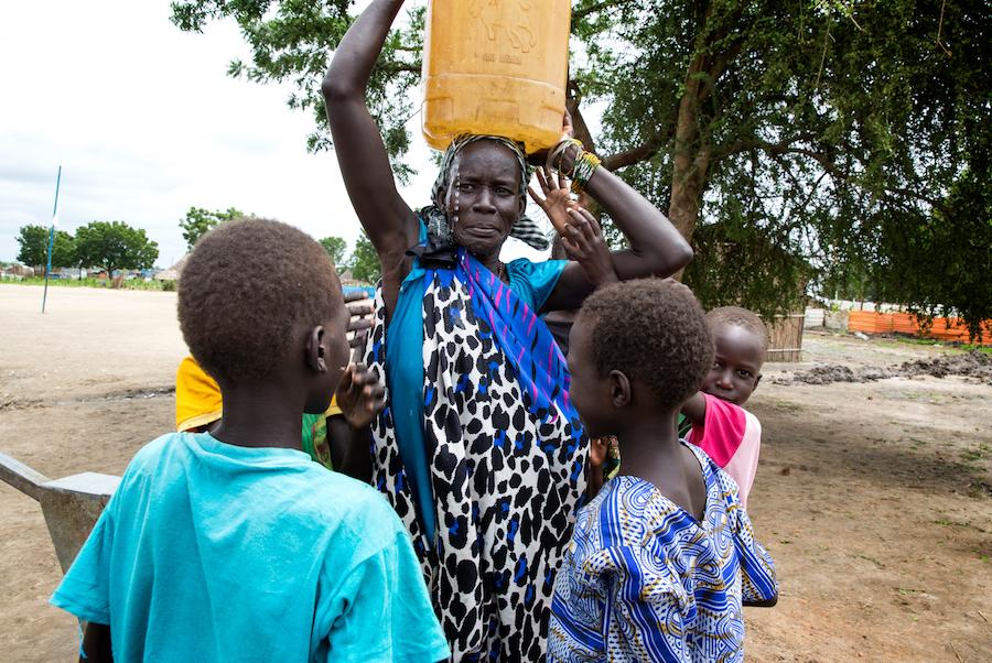 Angelina Nyakuma is surrounded by her children as she carries a jerry can of safe drinking water, drawn from a water pump at the Machakos Primary School, Bentiu, South Sudan, July 2017.