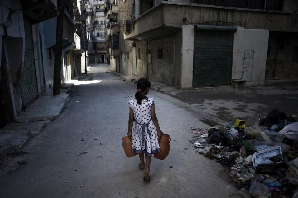 A girl, carrying jerrycans of water, walks past a pile of debris, on a street in Aleppo, capital of the north-western Aleppo Governorate. The city, which has been a site of prolonged fighting during the conflict, is experiencing frequent interruptions in 