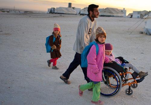 On 26 November 2013 in Jordan, Ahmed pushes his daughter Safa, 6, in a wheelchair through a refugee camp.