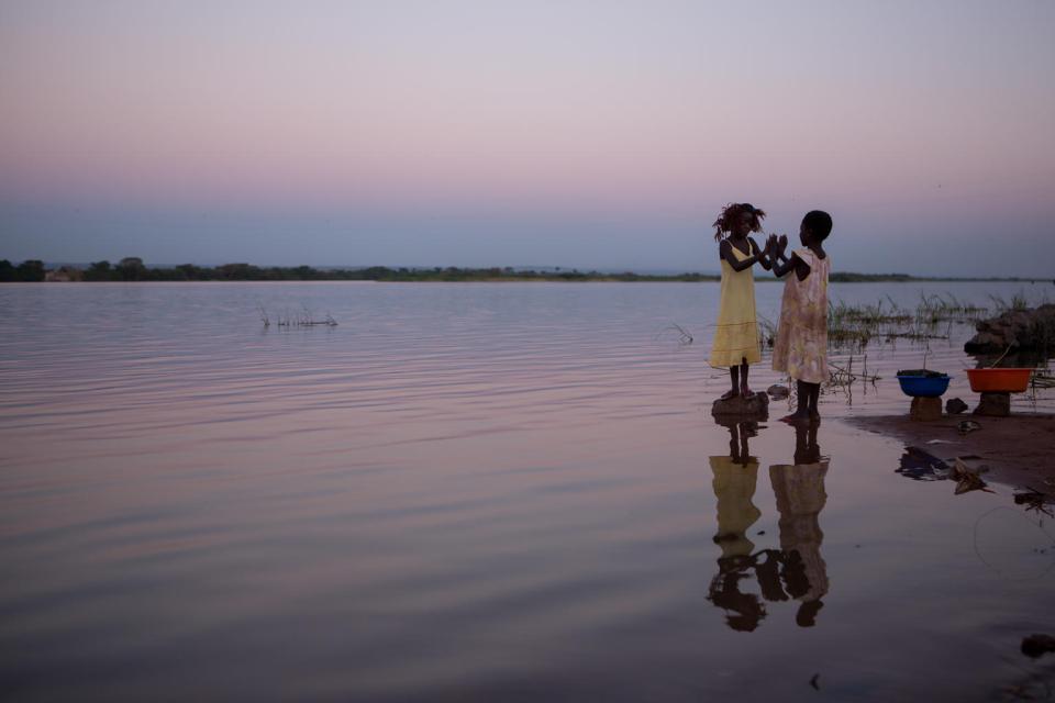 Two young girls play happily on the banks of the Luapala river at sunset in the Democratic Republic of the Congo. 