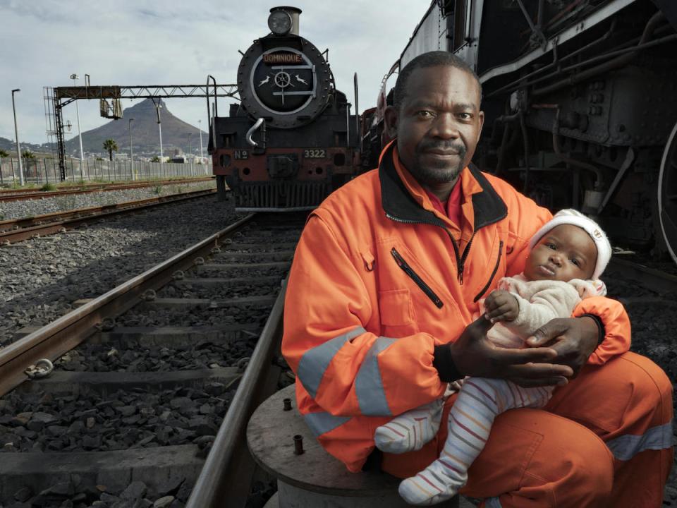 In May 2019, Congolese refugee Dieu-Merci Matala, 44, holds his infant daughter, Grace, near the Transnet harbor facility where he works in Cape Town, South Africa. 