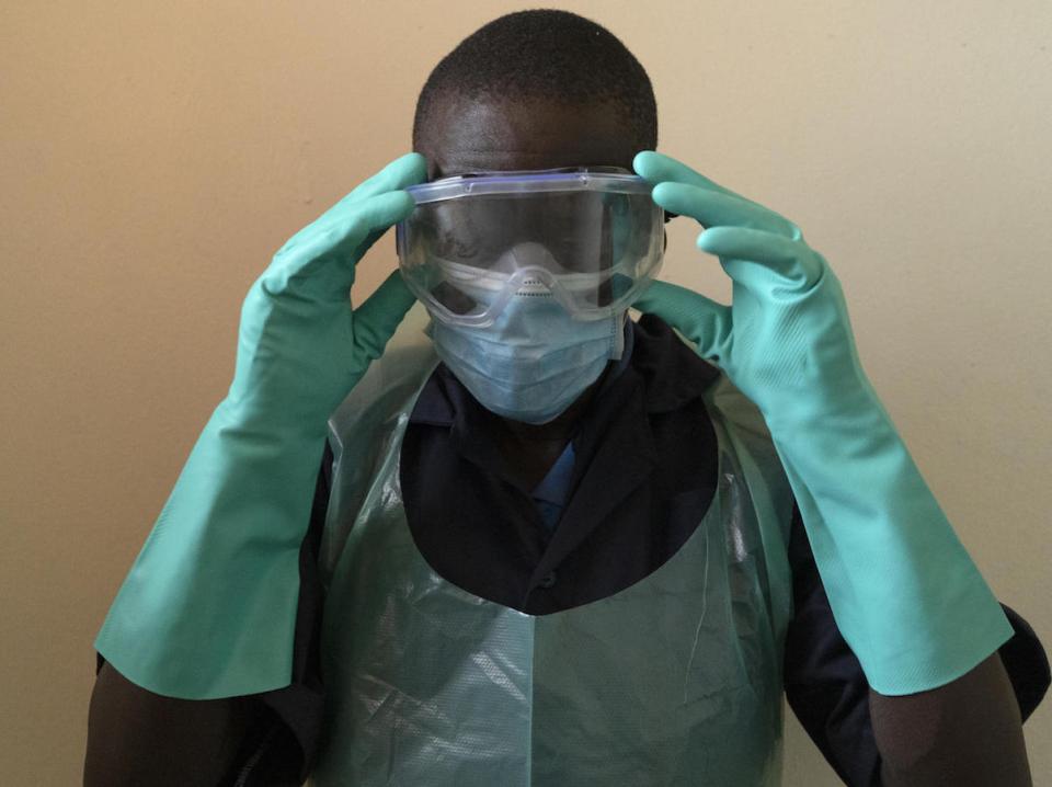 Yusto Katahoire puts on his personal protective equipment before starting his shift as Chief Hygienist at Kikuube Health Center IV, Kikuube District, Uganda. 
