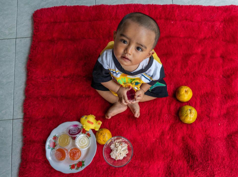 Eight-month-old Sakha holds a cup of dragon fruit pudding at his home in Pasung Village, Klaten, Central Java Province, Indonesia on September 7, 2021. 