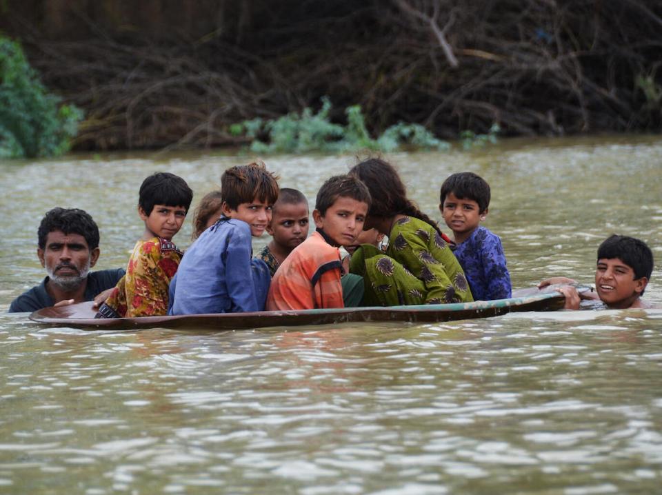 On Aug. 26, 2022, a man and a youth use a satellite dish to move children across a flooded area after heavy monsoon rainfalls in Jaffarabad district, Balochistan Province, Pakistan.