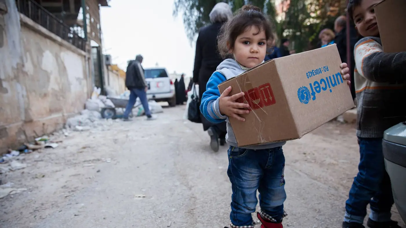 A young girl in Al-Waer, Homs, Syria, carries a box of winter clothes provided by UNICEF.