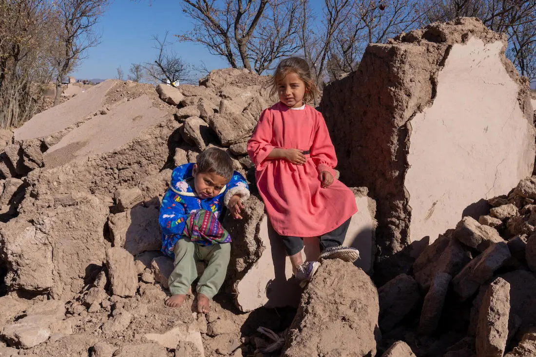 On Dec. 3, 2023, children sit for a portrait on a pile of rubble where their home used to stand in earthquake-affected Zinda Jan district, Herat province, Afghanistan.