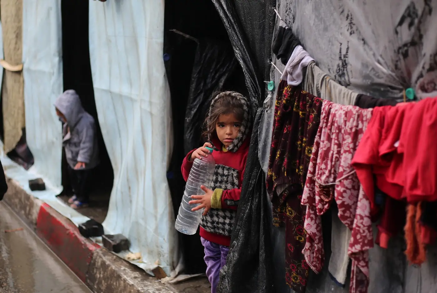 A little girl stands in front of her family's tent , holding an empty water bottle in the city of Rafah, southern Gaza Strip.