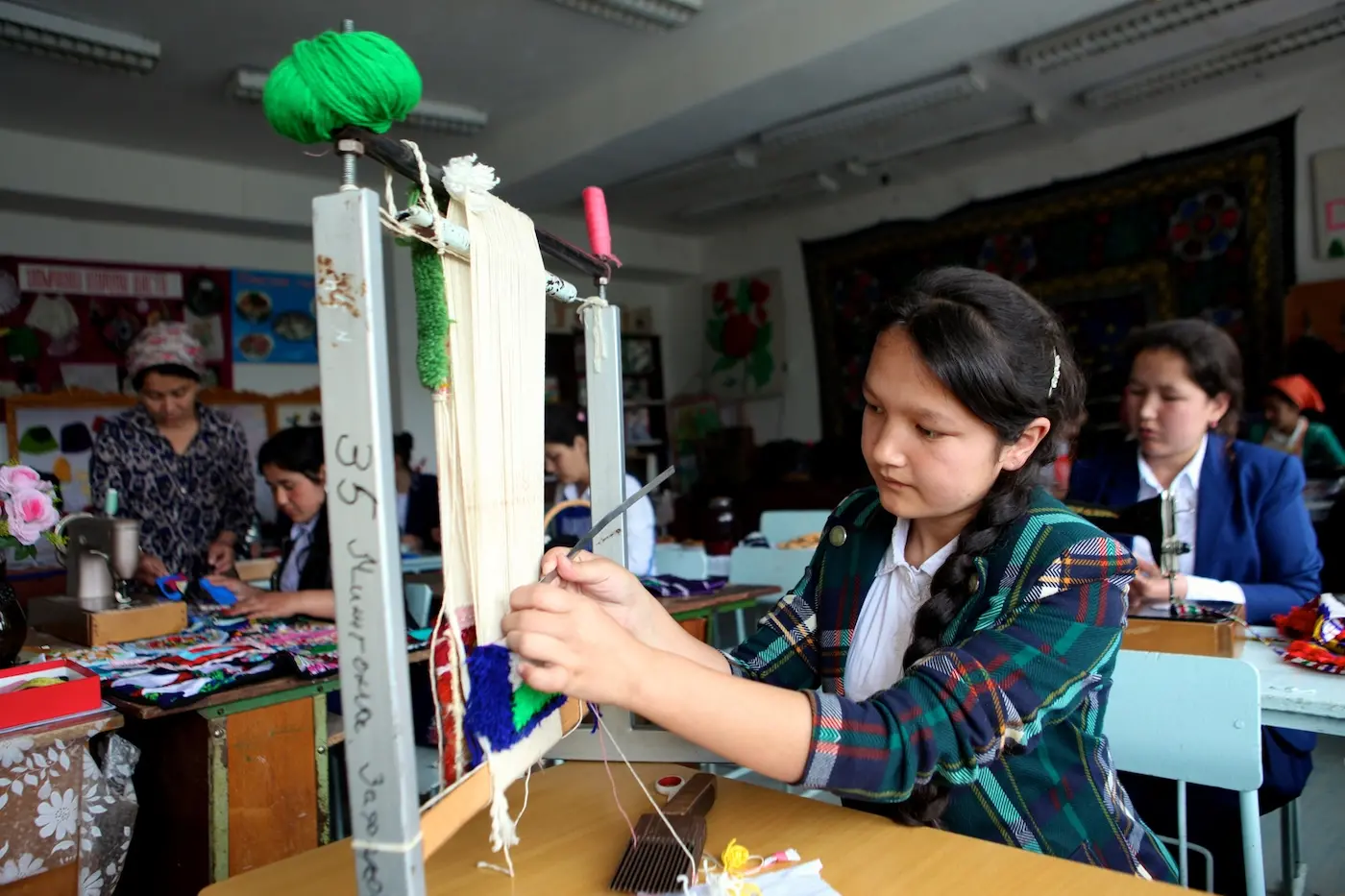 A girl weaves a carpet in her classroom 