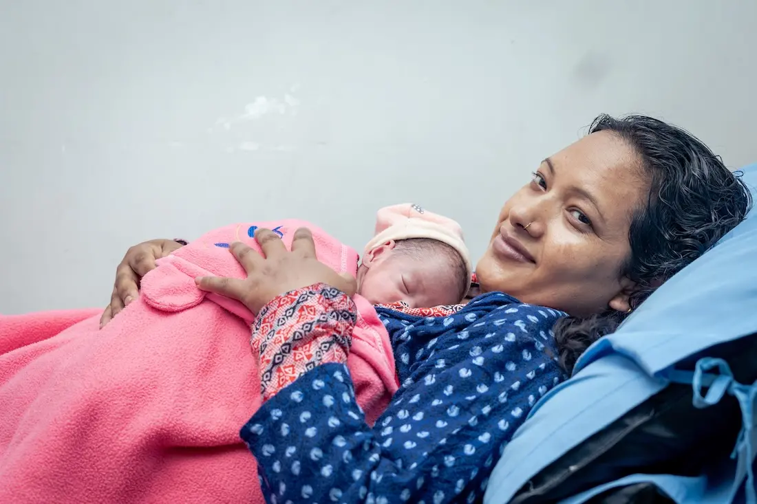 Mother cradles baby in hospital in Nepal where UNICEF supports newborn care.