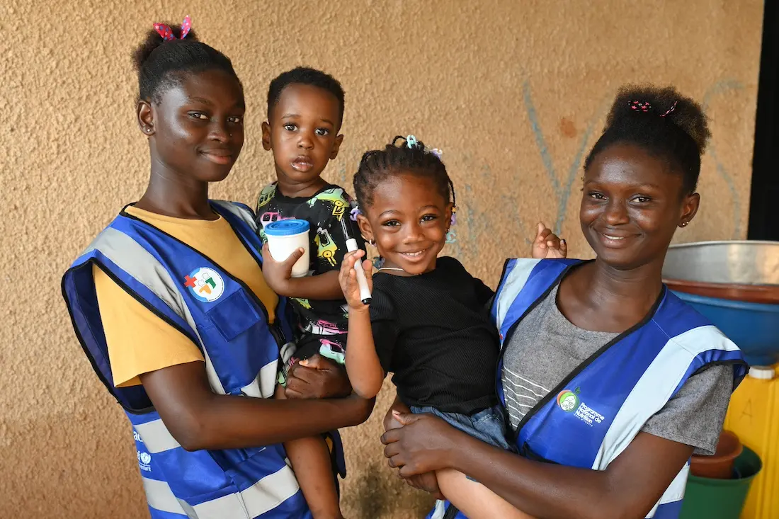 In Côte d'Ivoire, two nutrition workers hold two young children who just received Vitamin A supplements, an important UNICEF intervention..