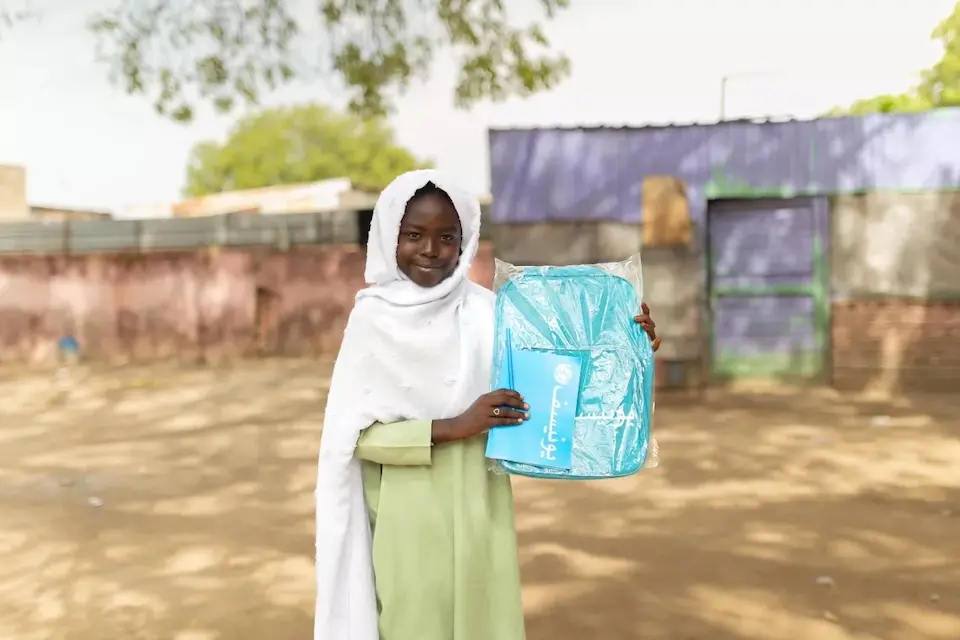 A smiling girl holds her new UNICEF backpack and notebook in Blue Nile State, Sudan.