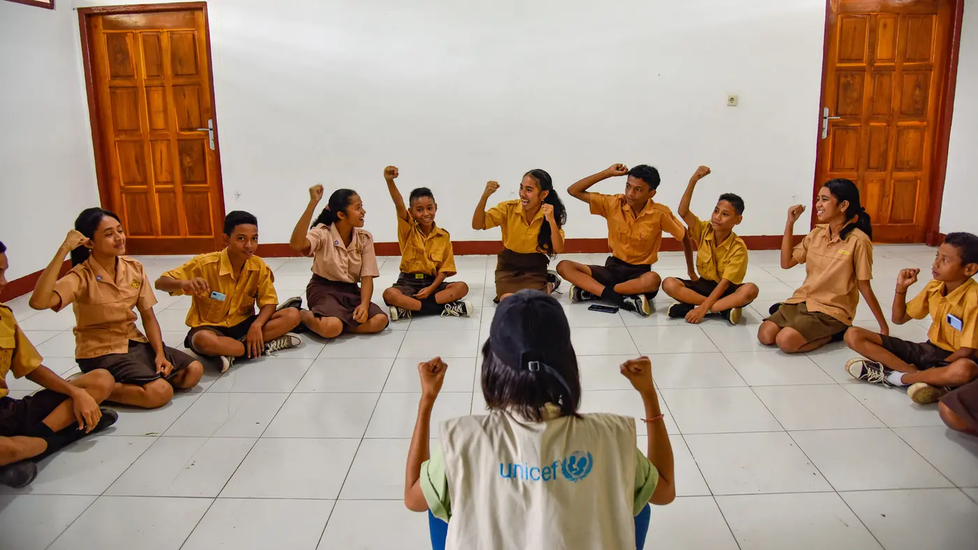 UNICEF worker in the middle of a half circle of smiling kids