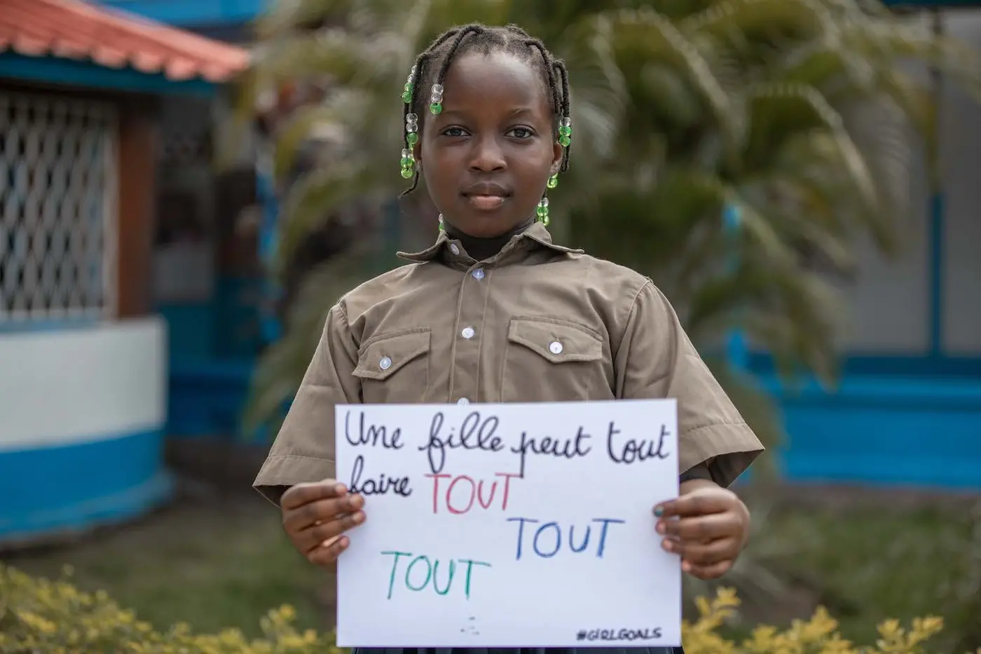 Eight-year-old Hadassah from the Republic of the Congo smiles at the camera holding a sign in French that says "girls can do everything."
