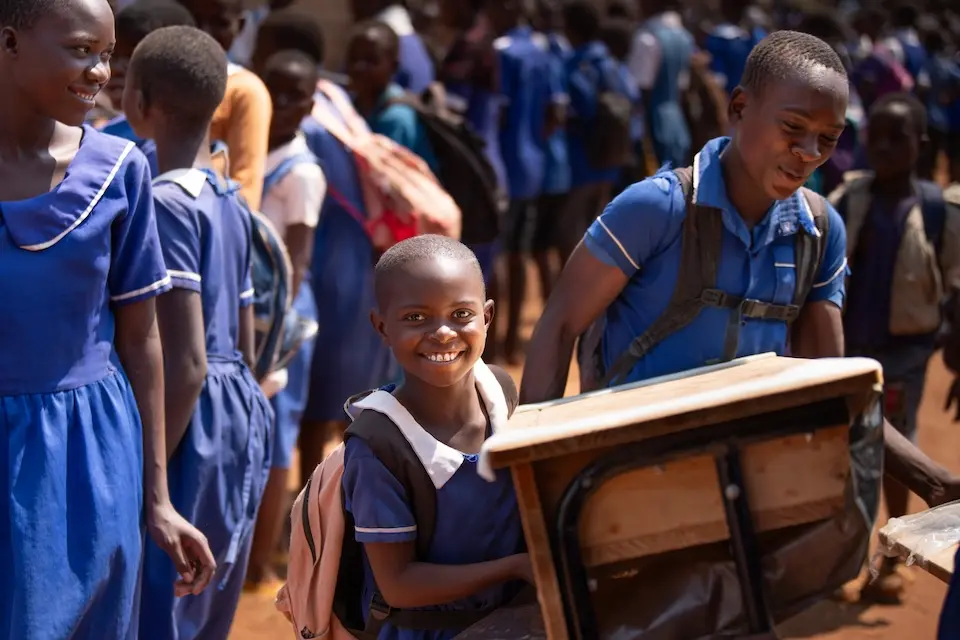 Students carry new desks from the K.I.N.D. Fund into their school in Malawi.