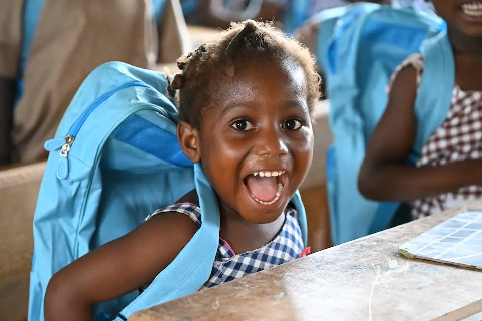 Smiling girl sitting at desk with UNICEF blue backpack on