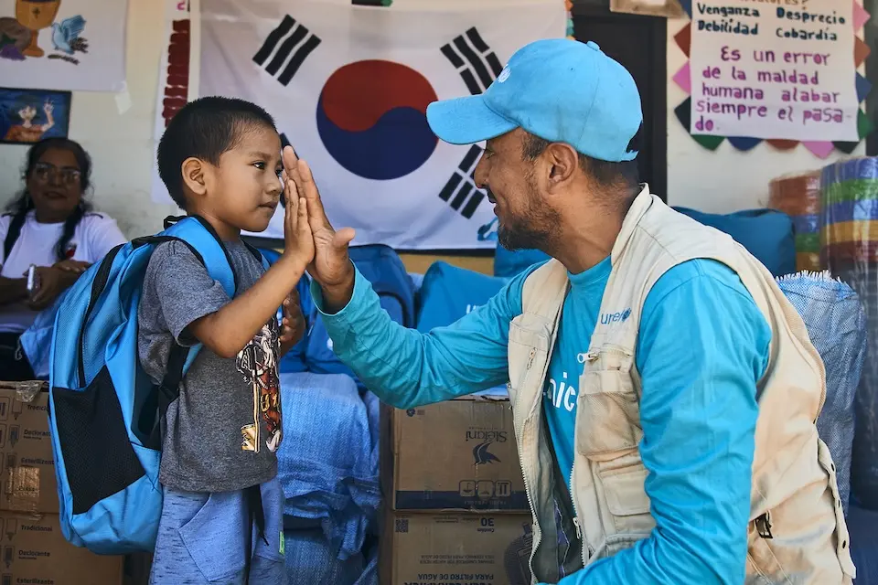 In Bolivia, a young boy who received a UNICEF backpack with school materials high-fives a UNICEF staff person.
