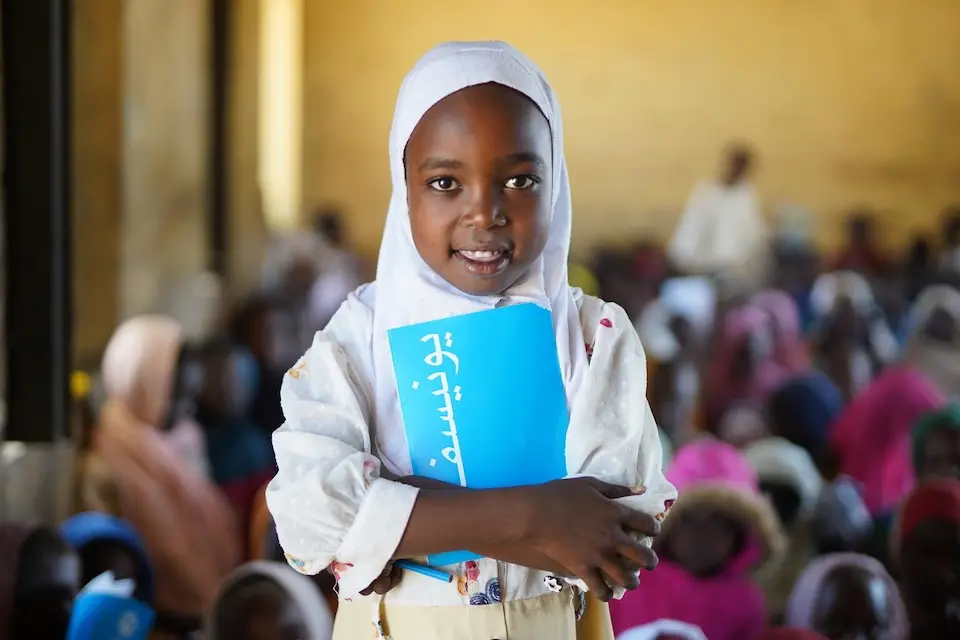 On Nov. 9, 2025, Aya, 7, holds a UNICEF notebook at a school in North Darfur, Sudan, where children who fled the war in Al Fasher received school supplies.