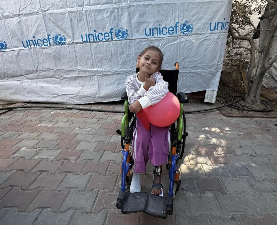 A girl in a wheelchair holds a balloon outside a UNICEF tent in central Gaza. 