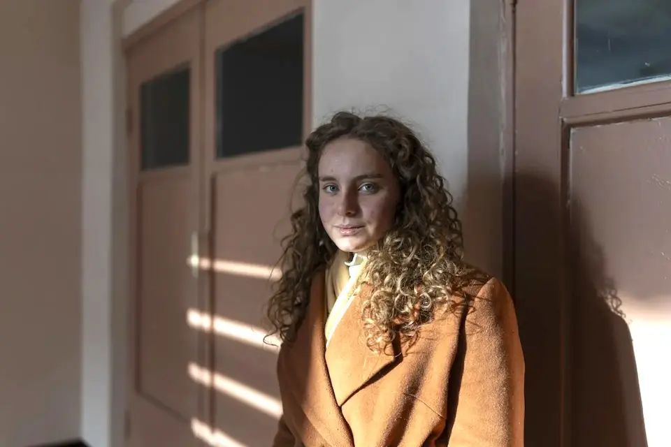 A 16-year-old girl in a winter coat stands outside a school classroom in Zlatopil, Ukraine.