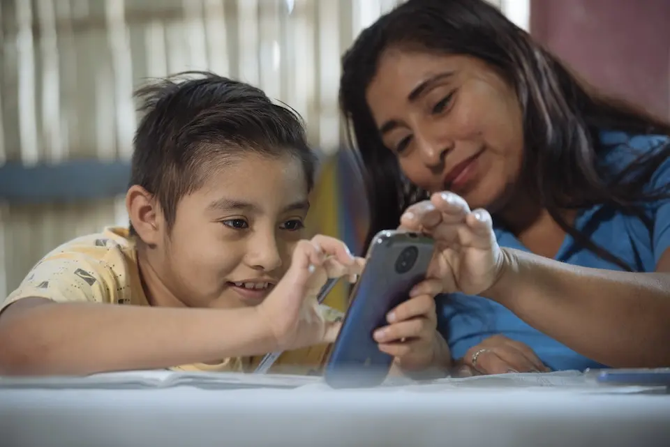 A mother in Ecuador helps her 9-year-old son with his homework using his cell phone.