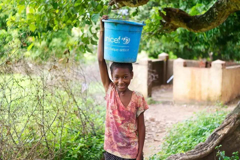 A young girl carrying a bucket of water donated by UNICEF on her head in Madagascar. 