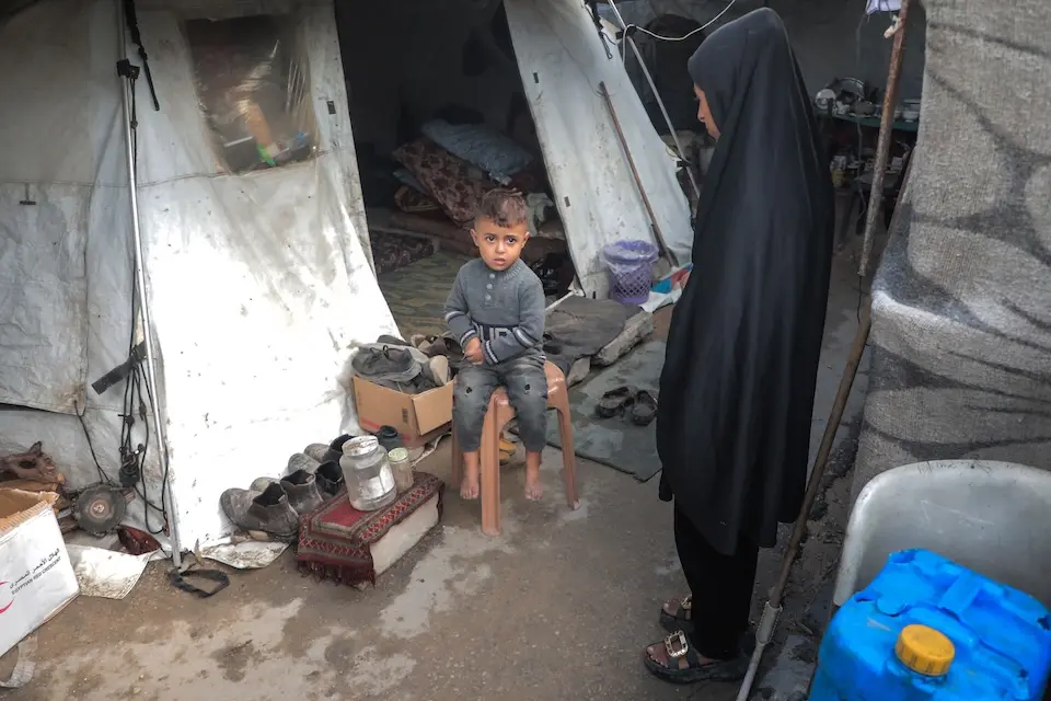 In Gaza, a small child sits by his mother outside their flooded tent.