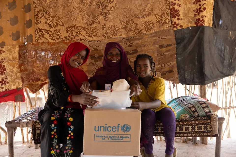 A mother and her daughters open a box containing UNICEF dignity kits in Aldamer, River Nile State, Sudan.
