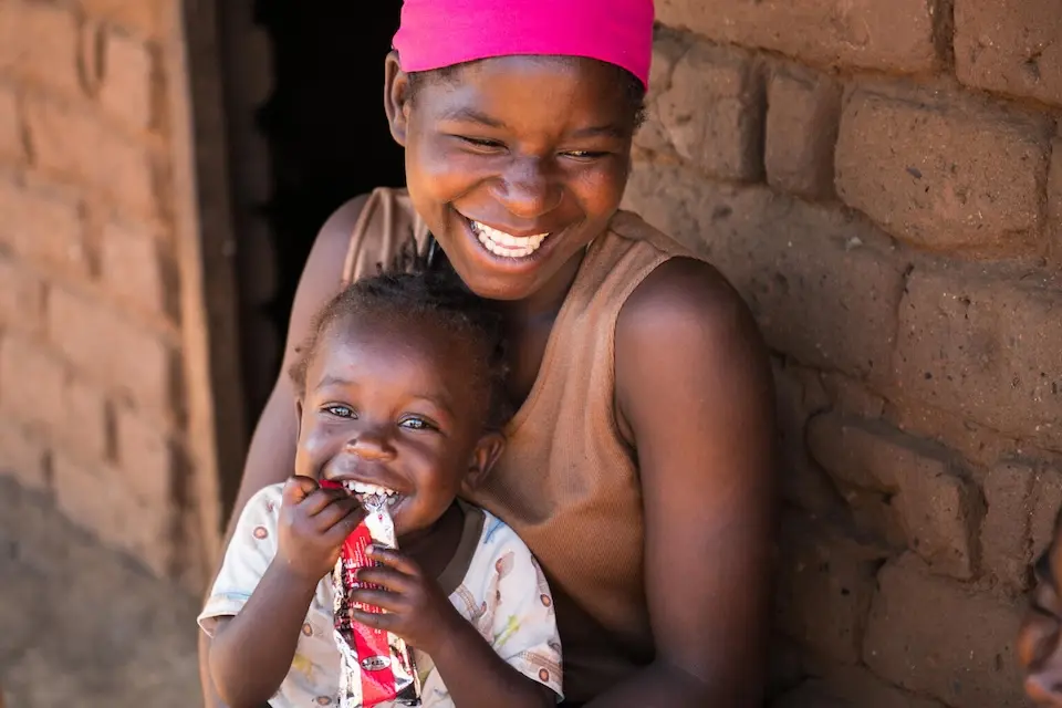 Edna Maunde, 20, smiles as her daughter, 2-year-old Christina, eats RUTF at their home in Mavila Village, Zomba, southern Malawi, on June 8, 2023.