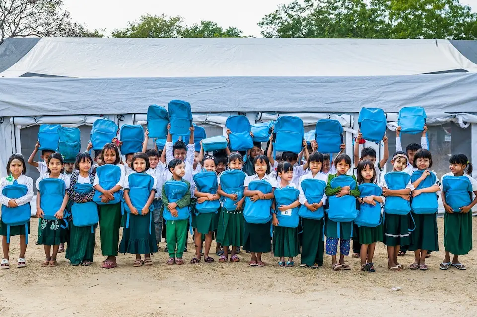 Children hold UNICEF backpacks outside a school tent at BEHS Pyitharyar in Pyawbwe Township, Mandalay Region, Myanmar.