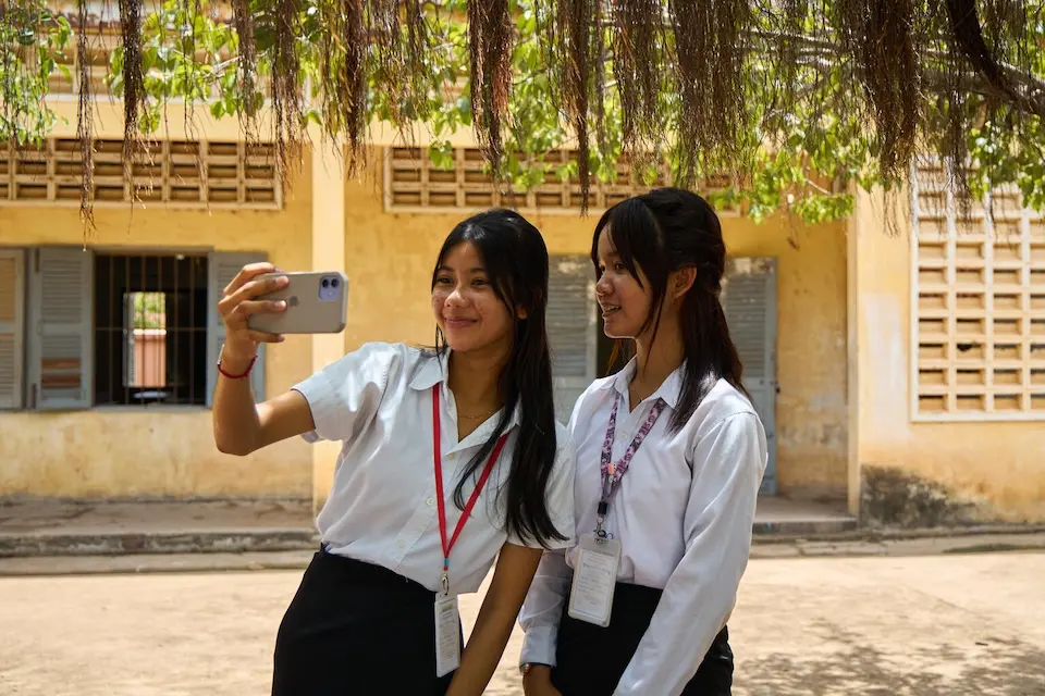 Two Grade 9 girls use social media on their phones outside their school in Battambang Province, Cambodia.  .