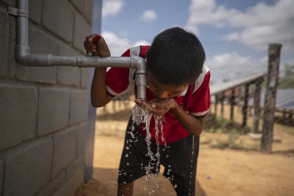 Young boy cups hands, drinking from spigot of clear water