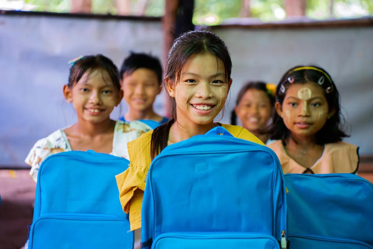 A group of girls in Myanmar proudly hold backpacks supplied by UNICEF. 