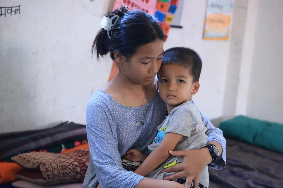 A 13-year-old girl holds her 3-year-old brother on her lap in Nepal.