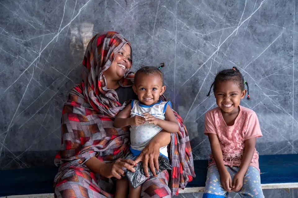 Woman holding small child, seated next to young girl, all smiling