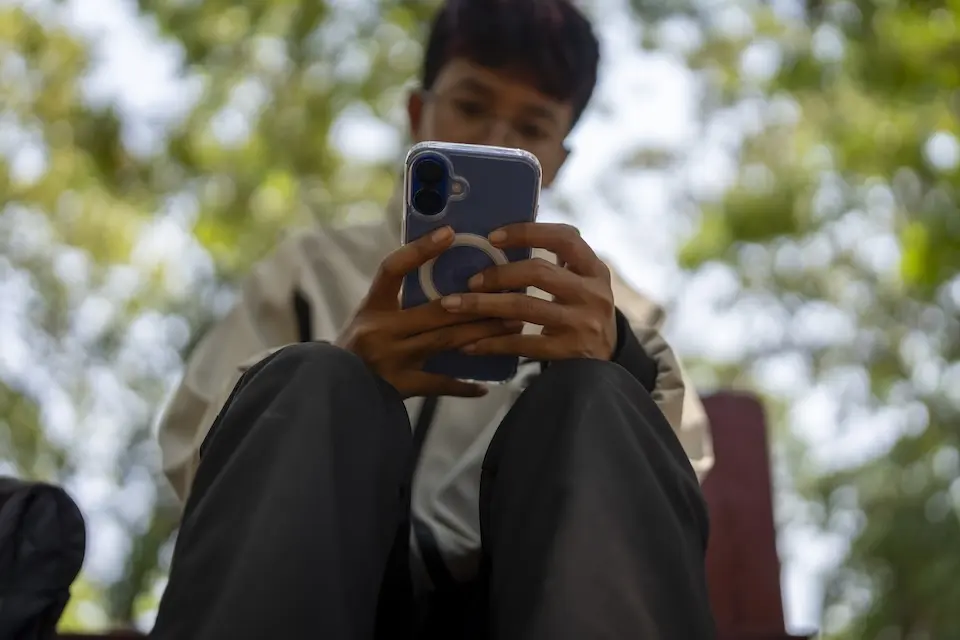 A young person scrolls through social media alone on a city street.