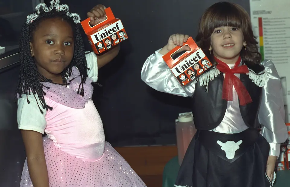 Two children in Halloween costumes hold their Trick or Treat for UNICEF boxes.
