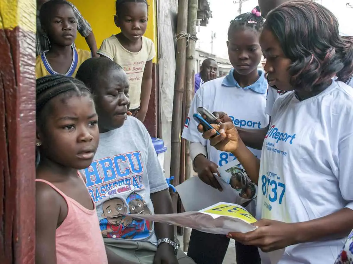 adolescent girls, holding brochures, read text messages on mobile telephones in the West Point neighbourhood of Monrovia, the capital. The girls, who are ‘U-Reporters’ are helping to raise awareness in the community about Ebola virus disease