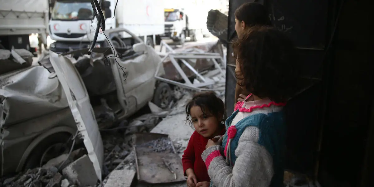 Children watch as a joint UNICEF, United Nations and Syrian Arab Red Crescent convoy of 46 trucks transporting food aid arrive in Eastern Ghouta on March 5, 2018.