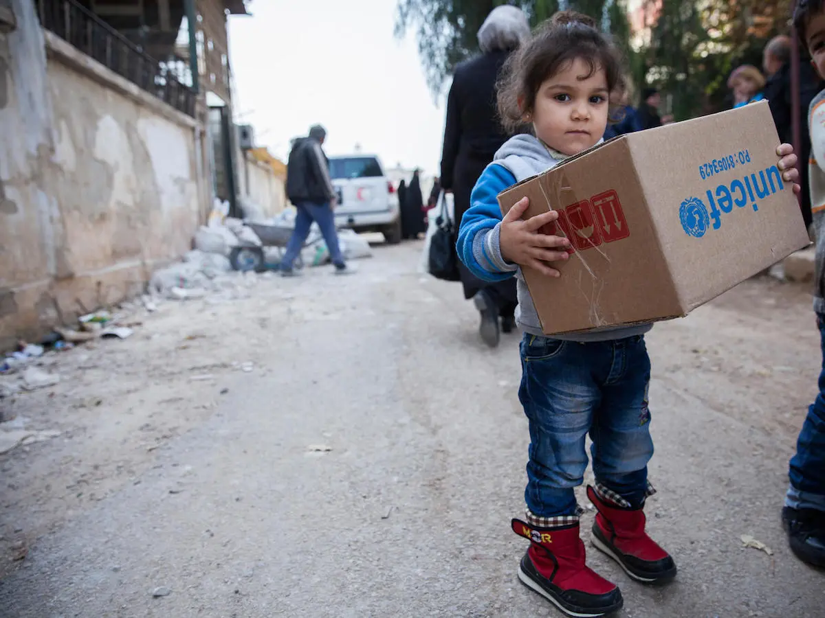 A child carries a box of winter clothes from UNICEF in Al-Waer, a neighborhood in Homs. UNICEF, Syria, humanitarian aid