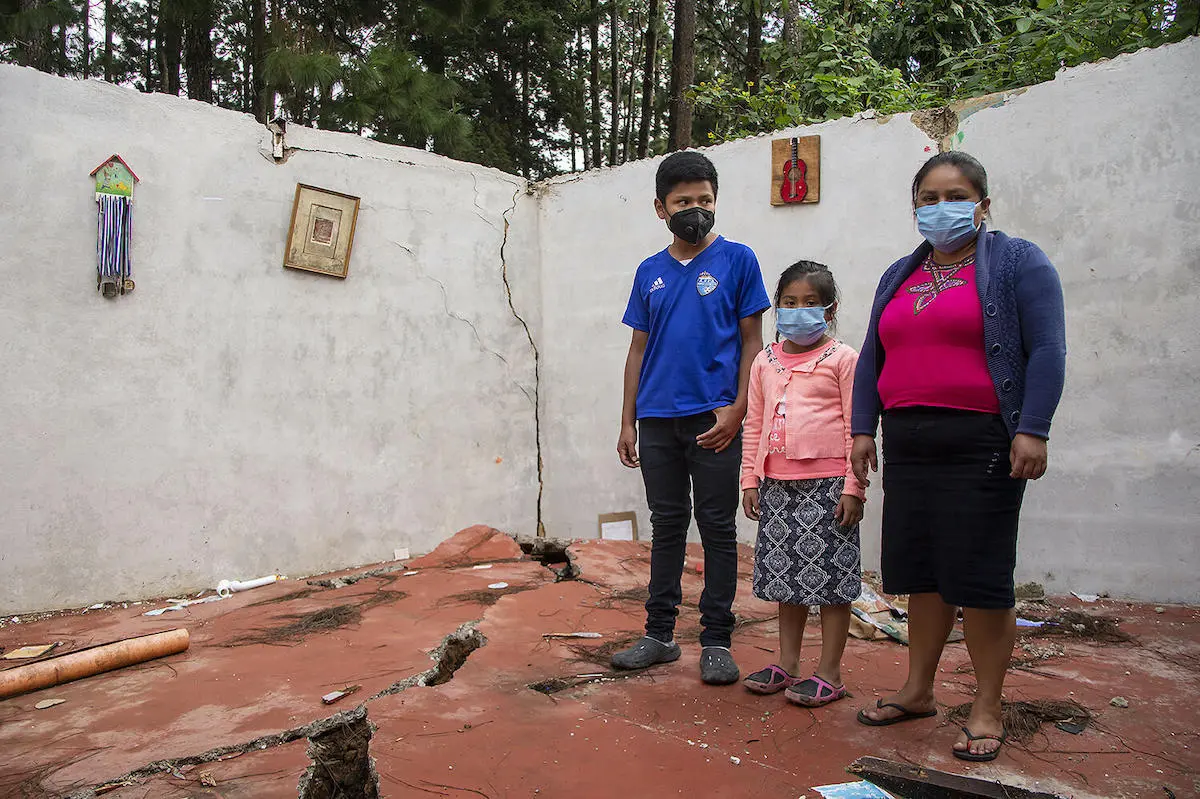 A mother with her two children stand in what remains of their home in Guatemala after storms Eta and Iota swept through, forcing them to flee to a temporary shelter.