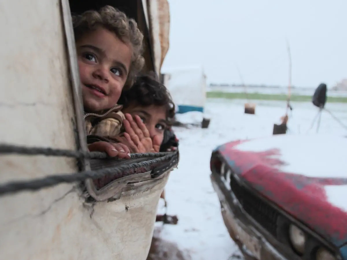 On 12 February 2020, children peer out from a tent at a recently established informal settlement which continues to receive newly displaced families from southern Idlib and rural Aleppo governorates in northwest Syrian Arab Republic.