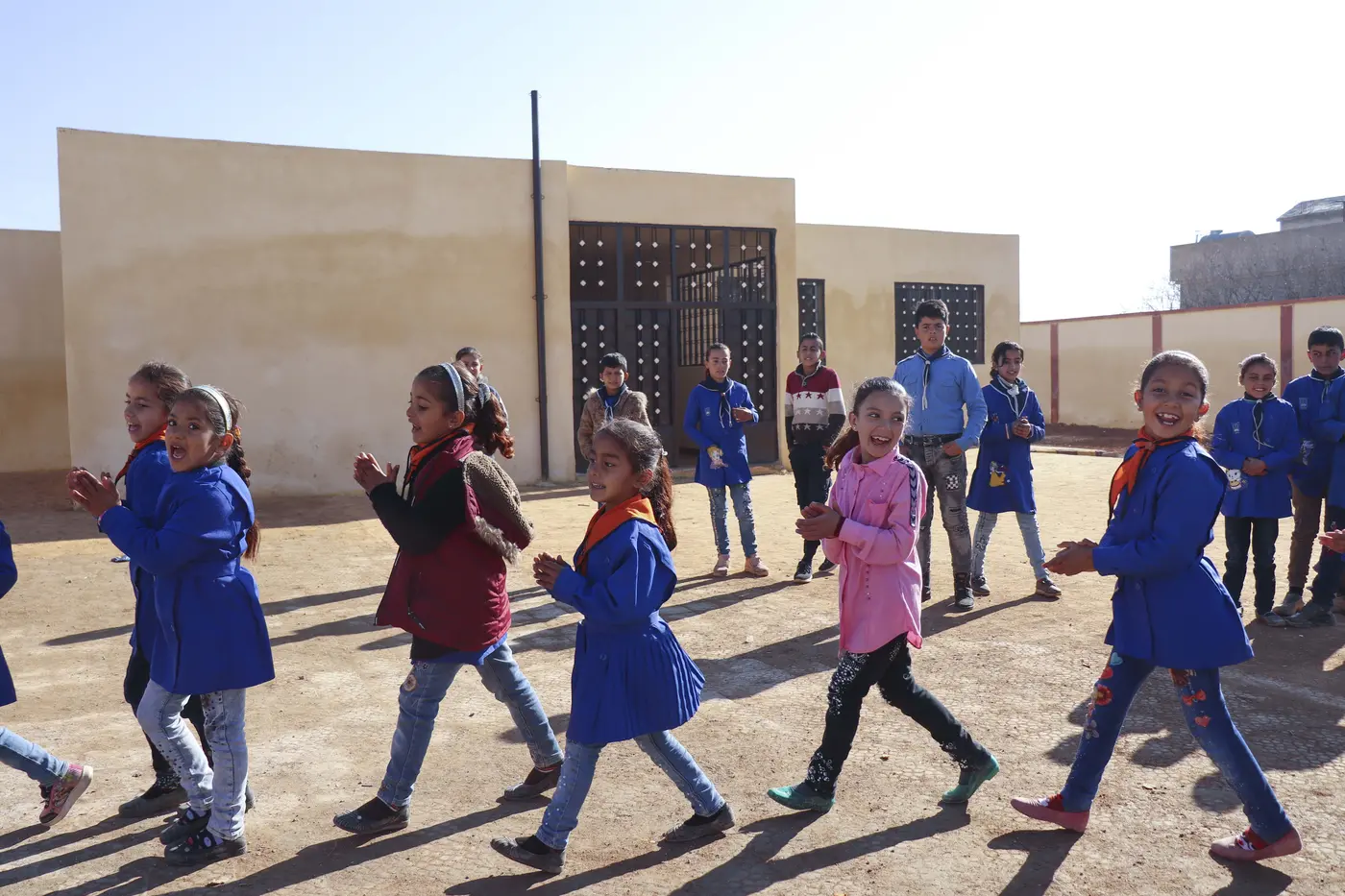 14 children smiling and playing outside in a sunny enclosed area. 