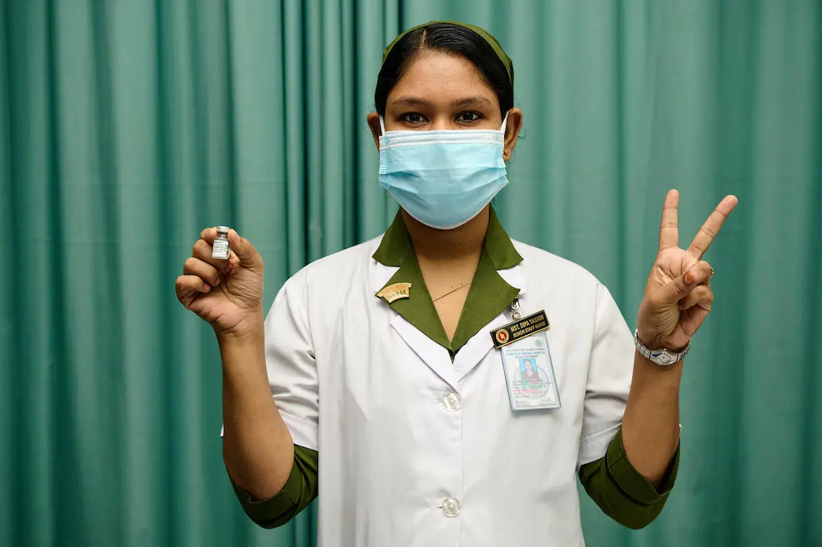 A trained vaccinator at Kurmitola General Hospital, Dhaka, Bangladesh, flashes V for victory — also V for vaccine — as COVID-19 vaccinations ramp up in the country, with support from UNICEF and the COVAX Facility.. A trained vaccinator at Kurmitola General Hospital, Dhaka, Bangladesh, flashes V for victory — also V for vaccine — as COVID-19 vaccinations ramp up in the country, with support from UNICEF and the COVAX Facility.