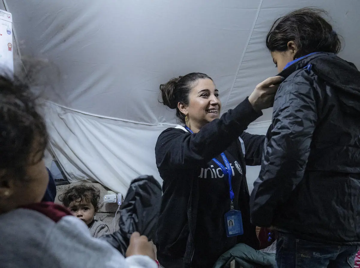 A UNICEF staffer helps a child try on a winter coat from a new winter clothing kit distributed by UNICEF and partners to families living in Roj IDP camp, northeastern Syria. 