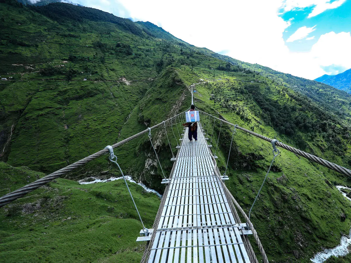 UNICEF-trained health worker Birma Kunwar crosses a suspension bridge in Nepal's Darchula District to deliver COVID-19 vaccine doses to a rural vaccination site.