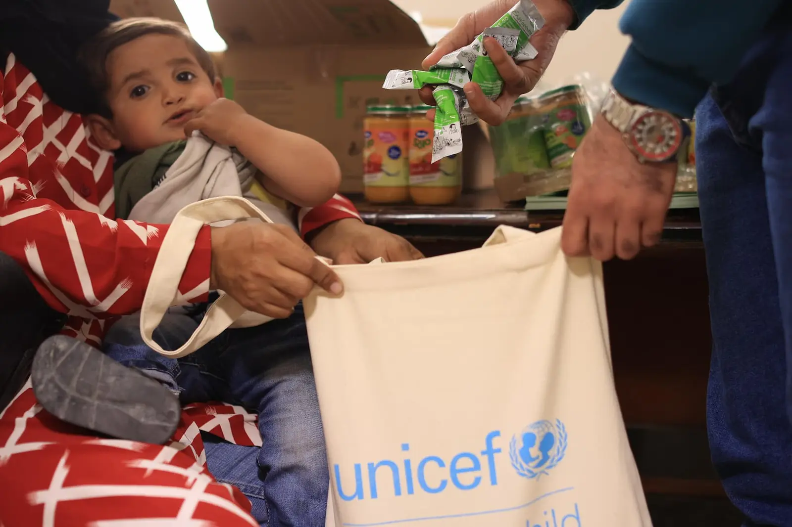 Child being held while a UNICEF bag is filled with food