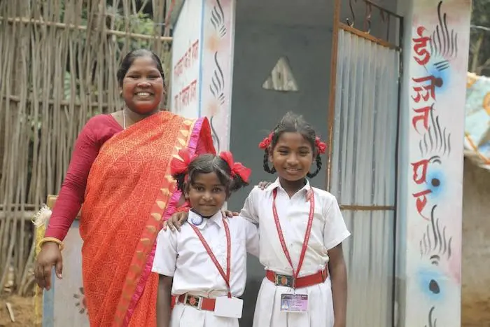 Alka Minj stands with her daughters outside a toilet she built in Jharkhand, India. She is paying for her daughters' education using her income as a mason. 