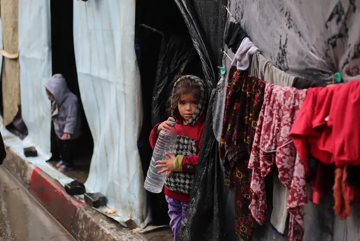 A little girl stands in front of her family's tent , holding an empty water bottle in the city of Rafah, southern Gaza Strip.