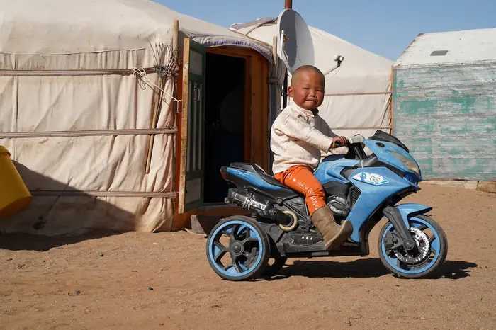 Ochir-erdene, 3, riding on his toy motorcycle in front of his herder family's ger home in a remote part of Dundgobi, Mongolia.
